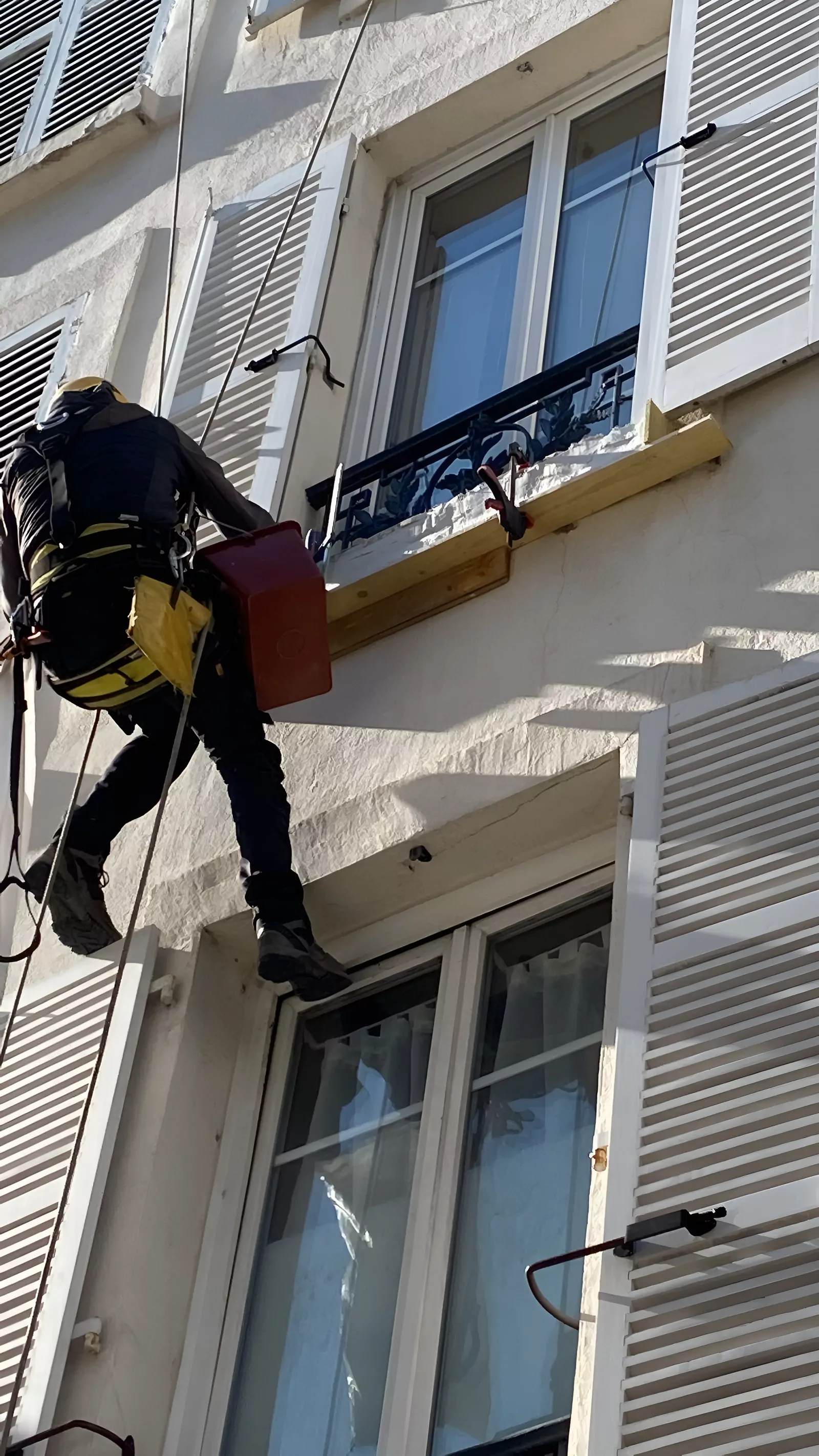 Cordiste intervenant à une fenêtre d'un immeuble à persiennes