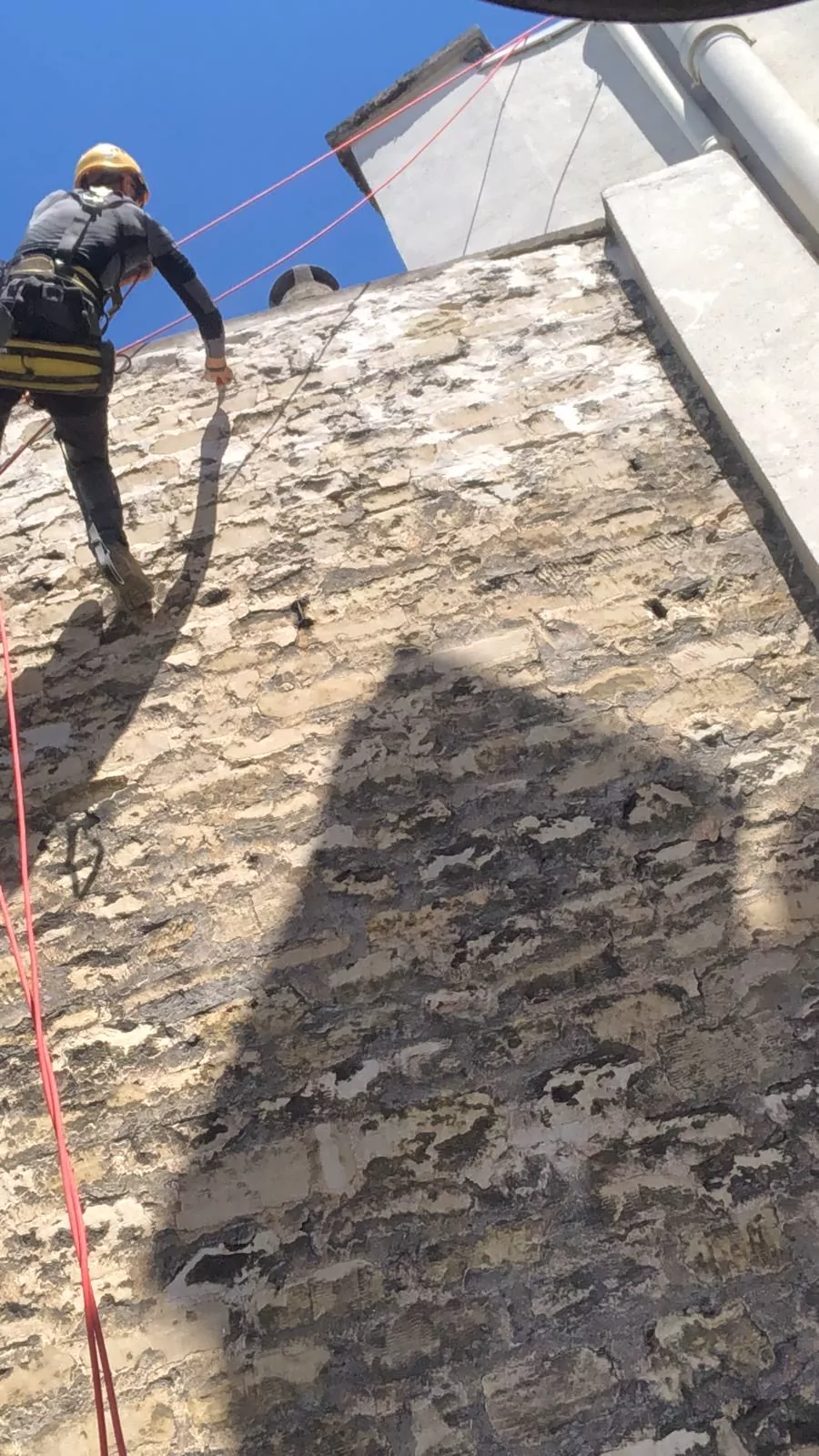 Cordiste sur un mur pignon en moellons à l'enduit dégradé