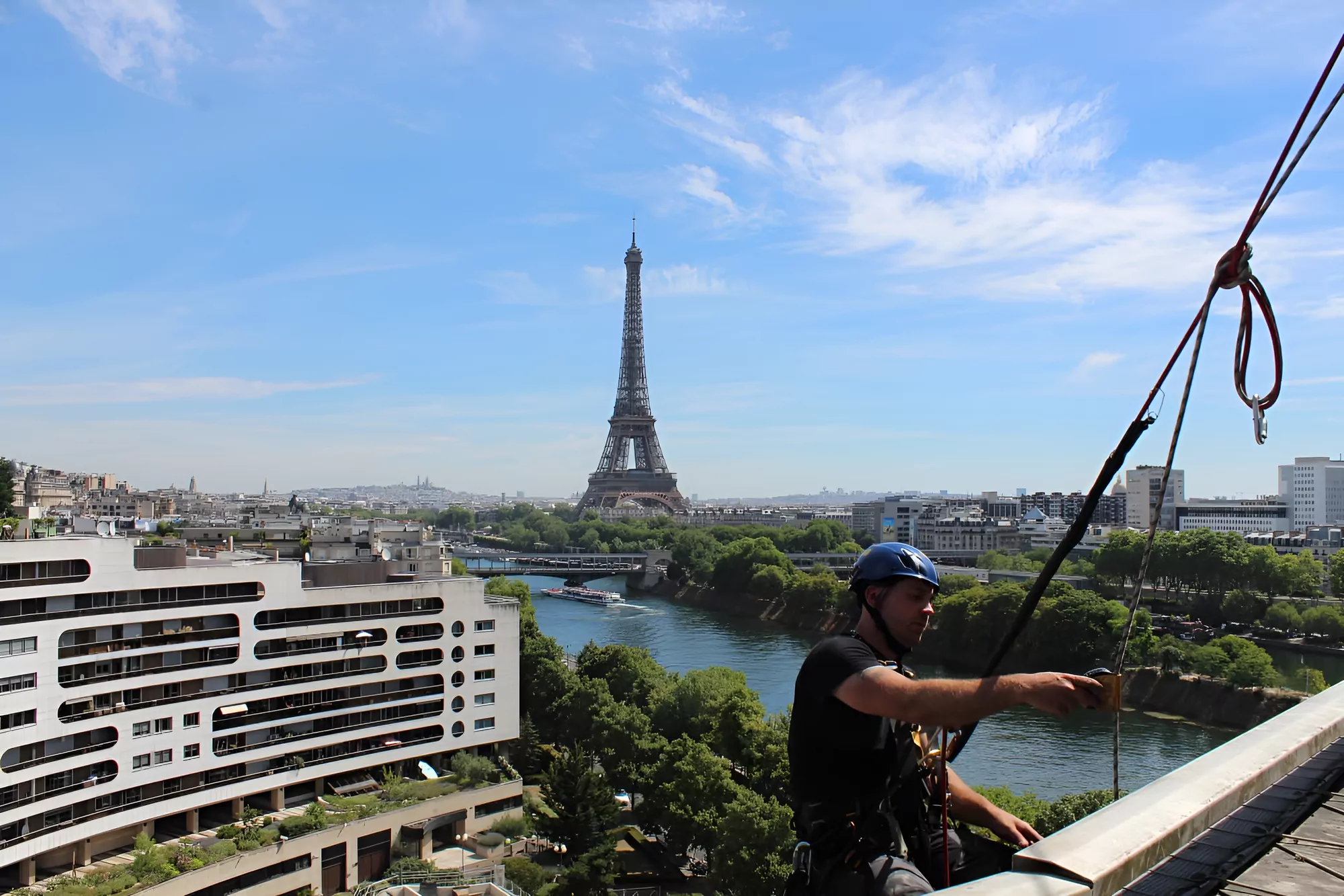 Cordiste réglant ses cordes sur un ancrage de toiture, face à la tour Eiffel