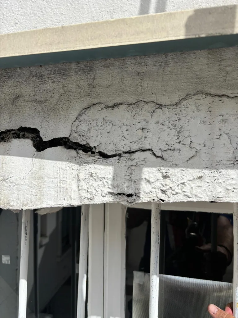 Fissure ouverte dans un bandeau de béton en façade, vue de près depuis les cordes