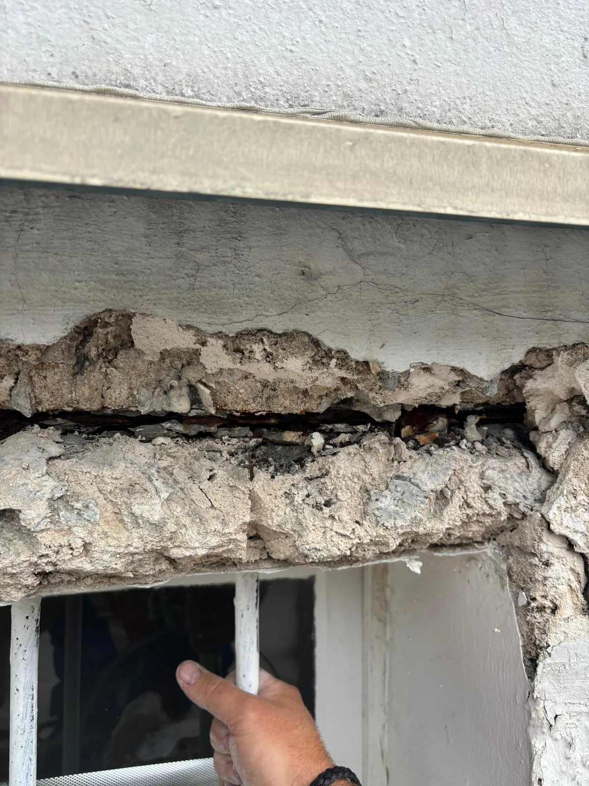 Éclat de béton en façade, aciers apparents et main du cordiste