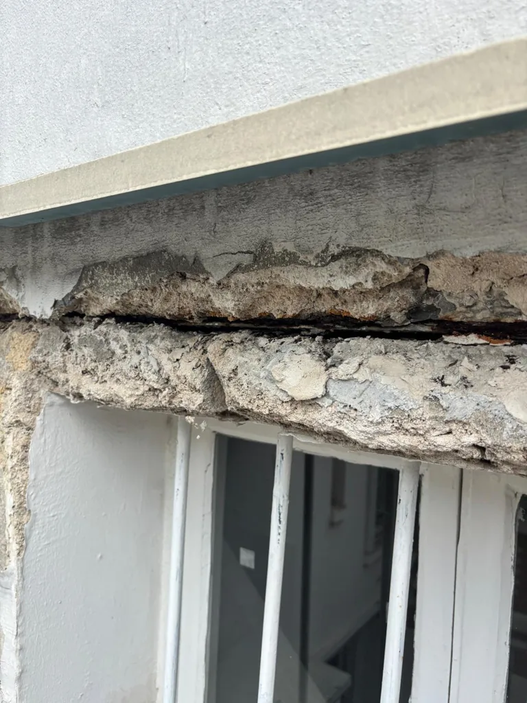 Bandeau en béton fissuré et éclaté au-dessus d'une fenêtre