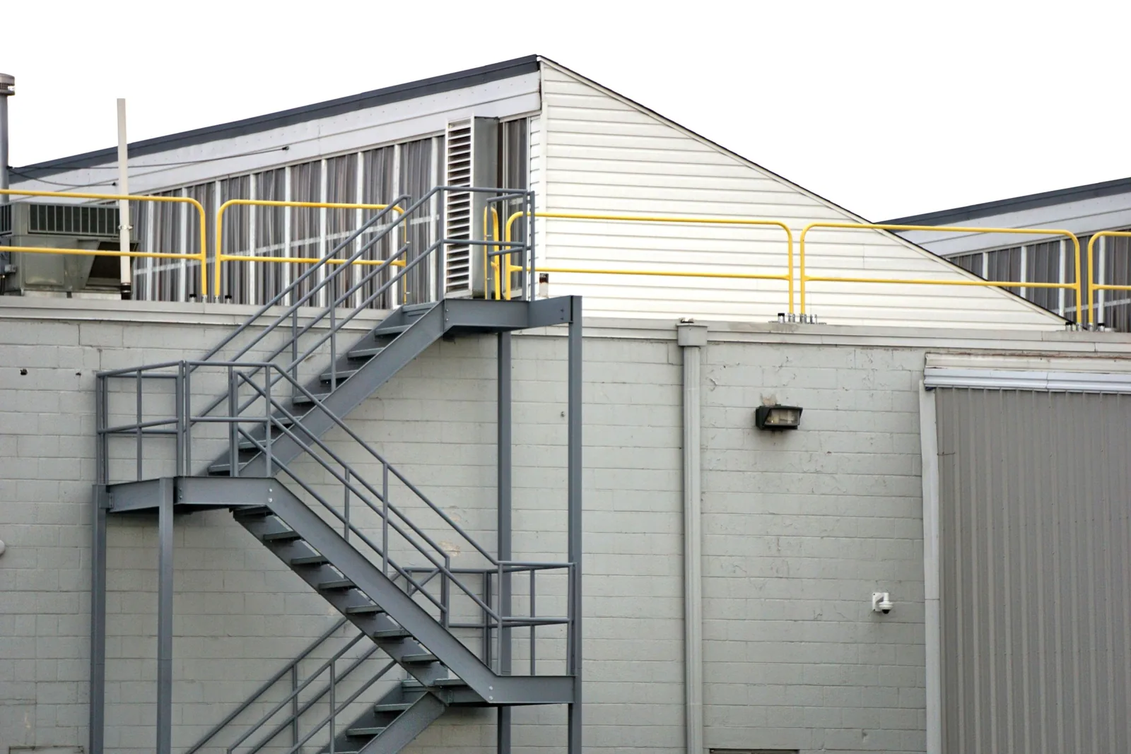 Escalier métallique d'accès et garde-corps jaunes d'un cheminement sur la toiture d'un bâtiment industriel