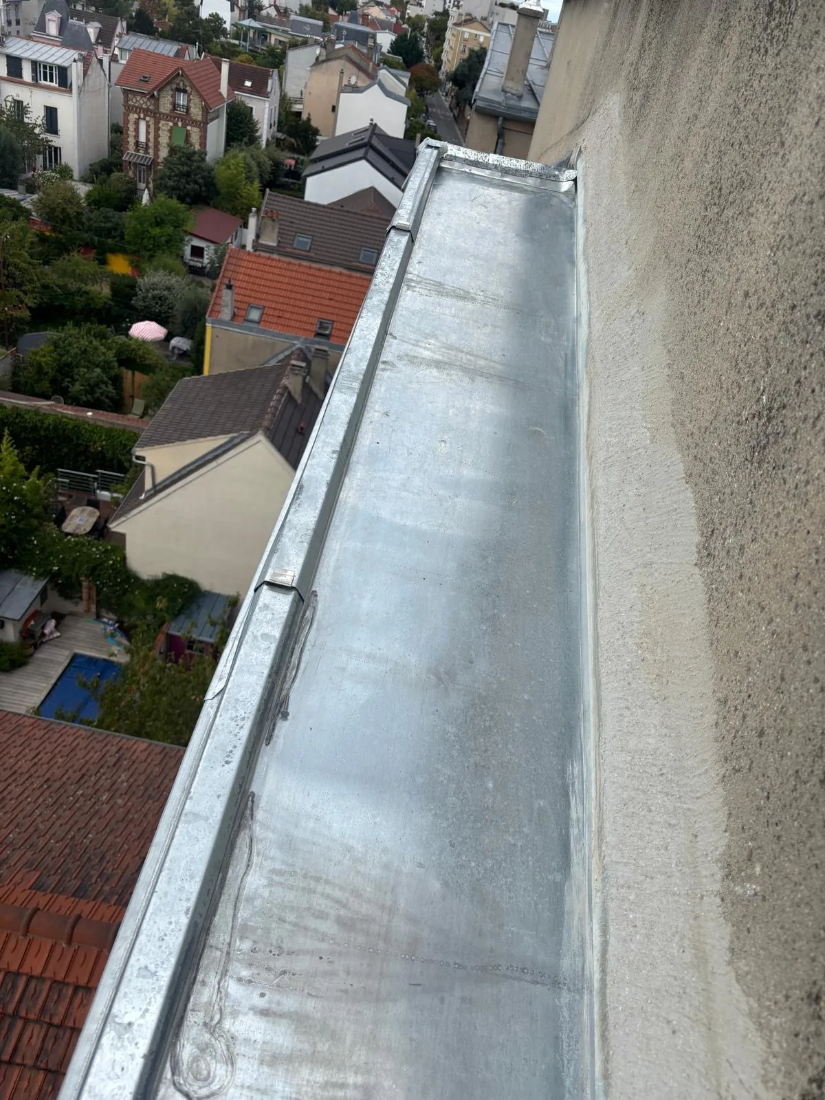 Chéneau en zinc neuf posé en tête d'un mur en pierre, vu depuis la toiture