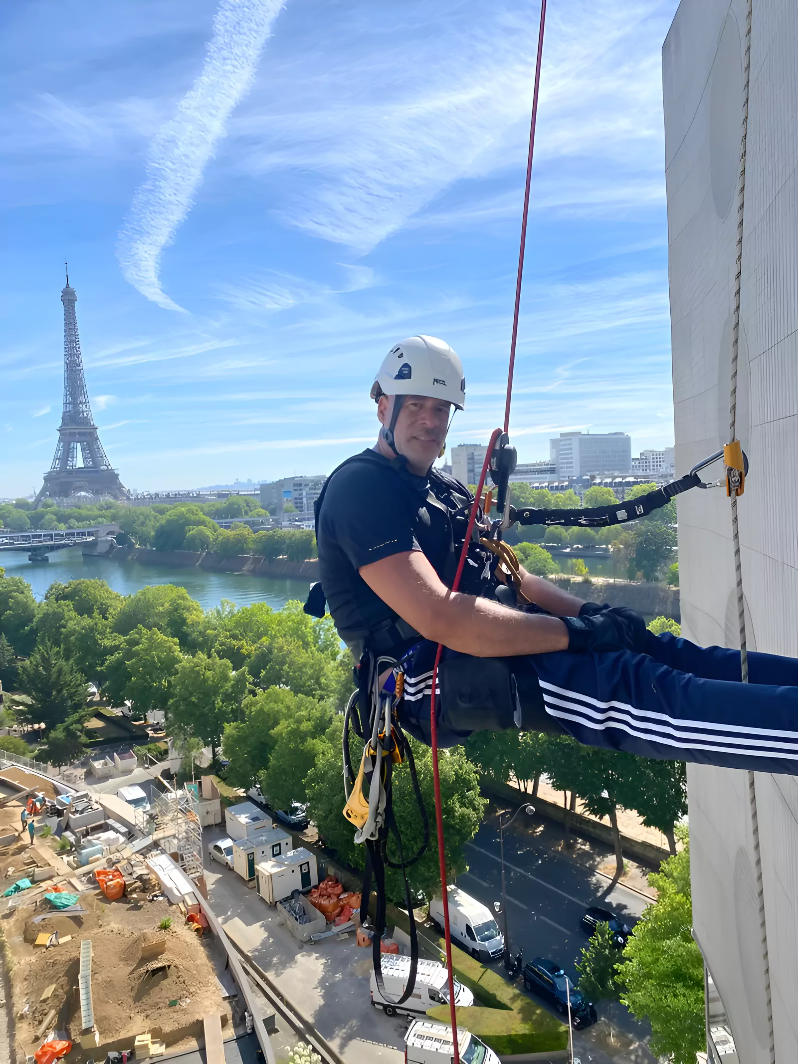 Cordiste suspendu en façade à Paris, la tour Eiffel en arrière-plan