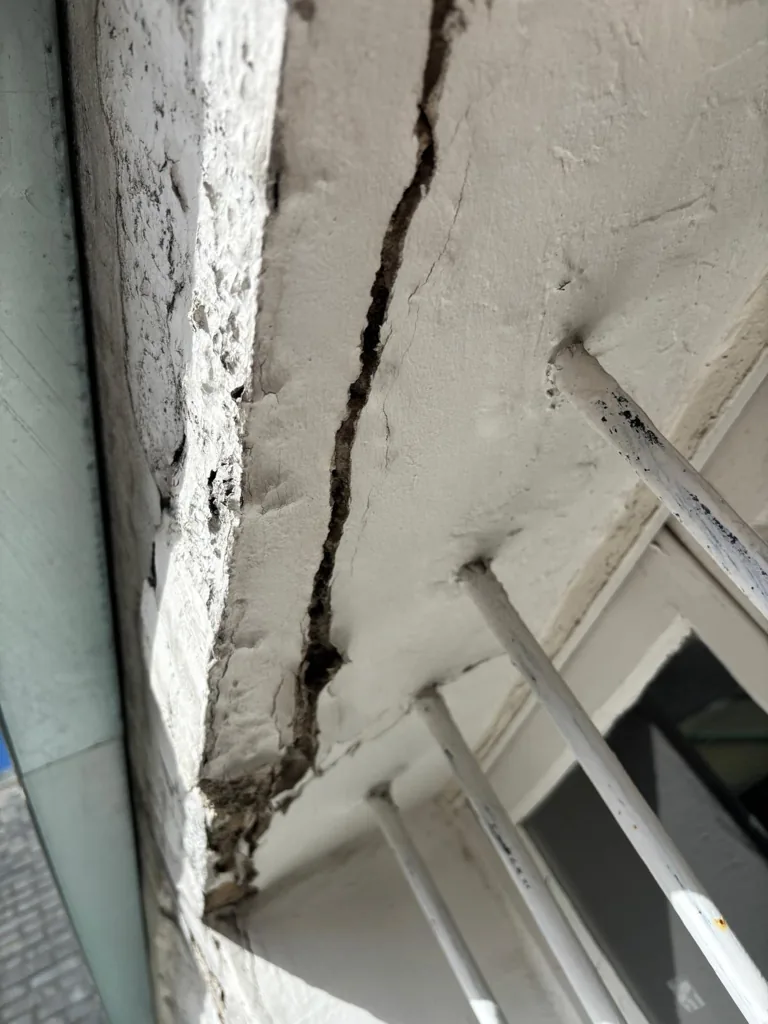 Angle de corniche en béton éclaté, fissure ouverte et aciers apparents