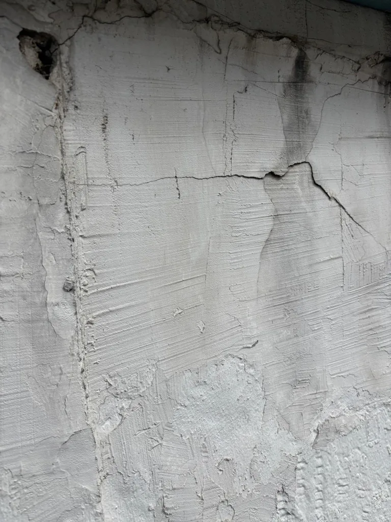 Fissure verticale dans le béton d'une corniche, enduit soulevé