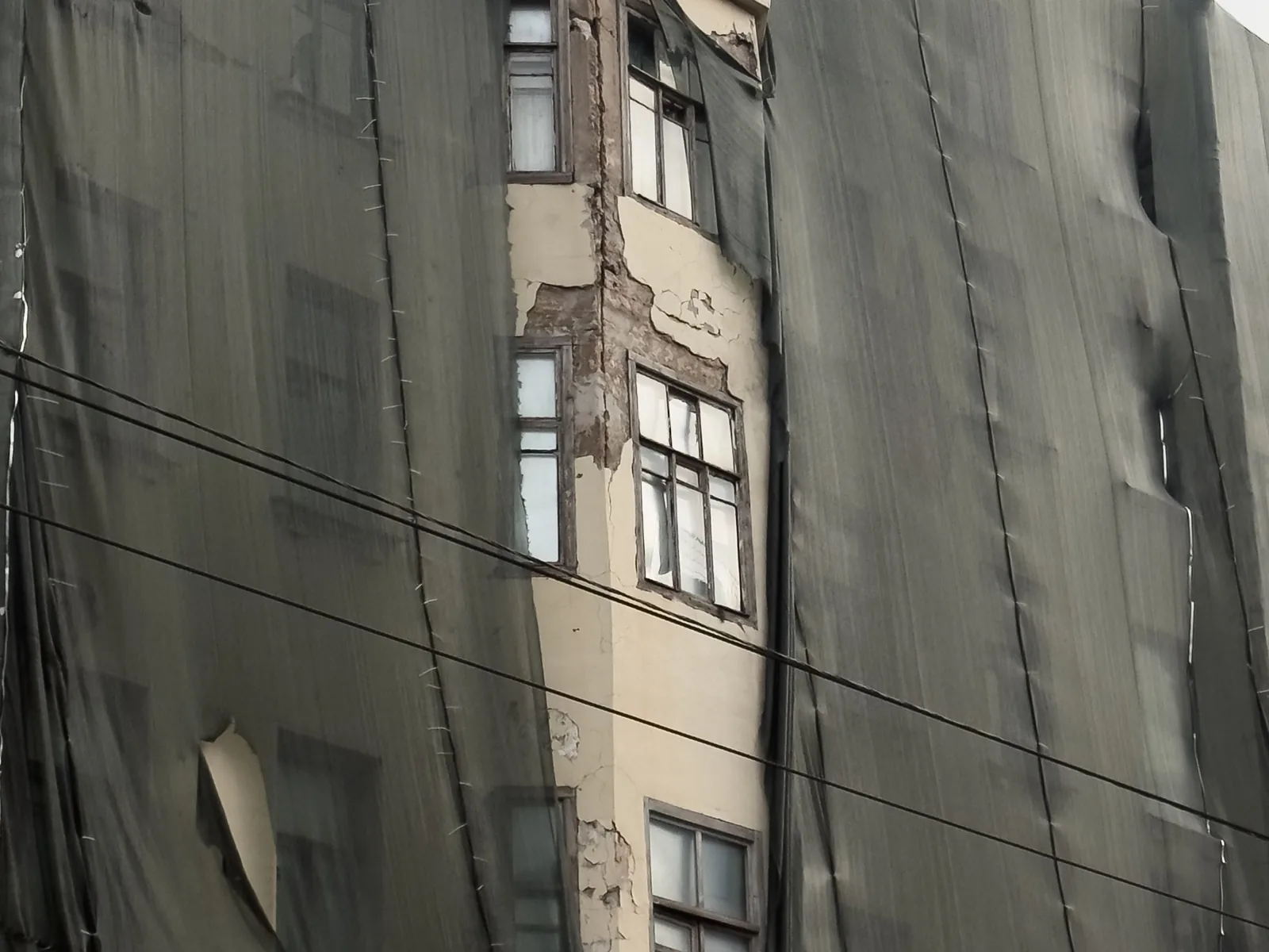 Filet de protection de façade en place depuis longtemps, détendu et déchiré devant les fenêtres d'un vieil immeuble
