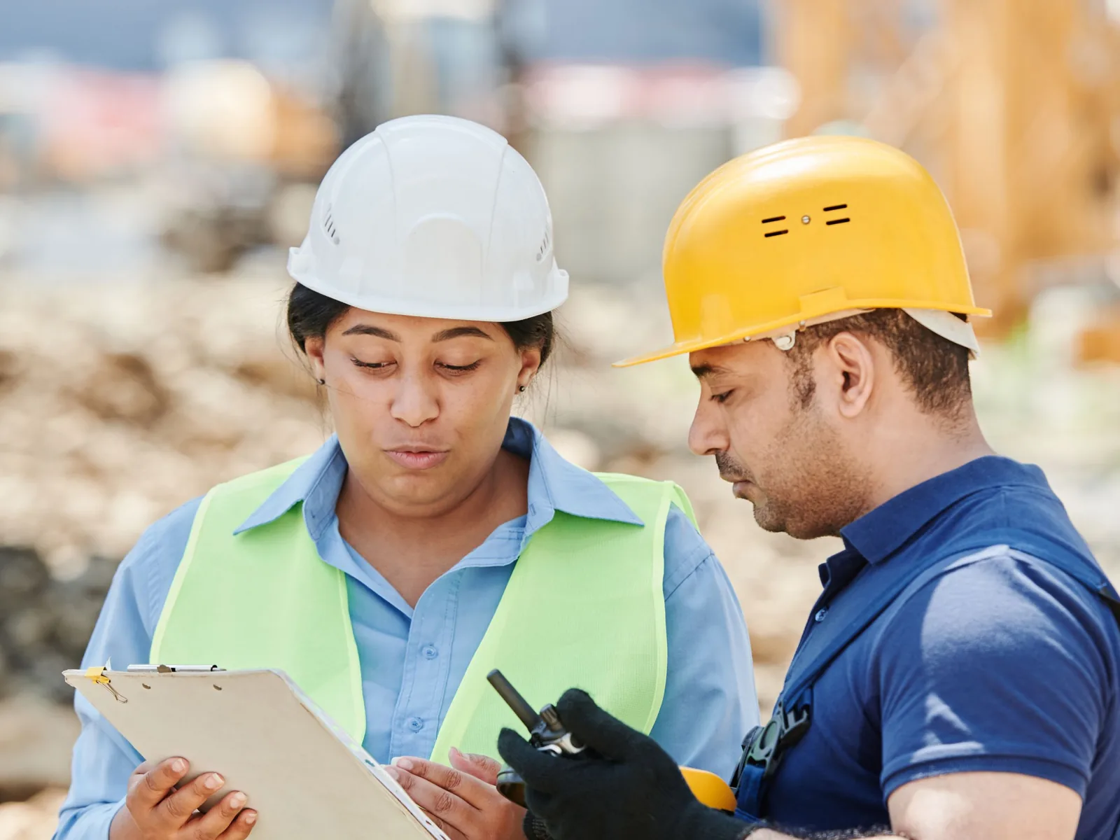 Deux responsables de chantier en casque et gilet examinent ensemble un document sur une planchette, inspection commune avant travaux