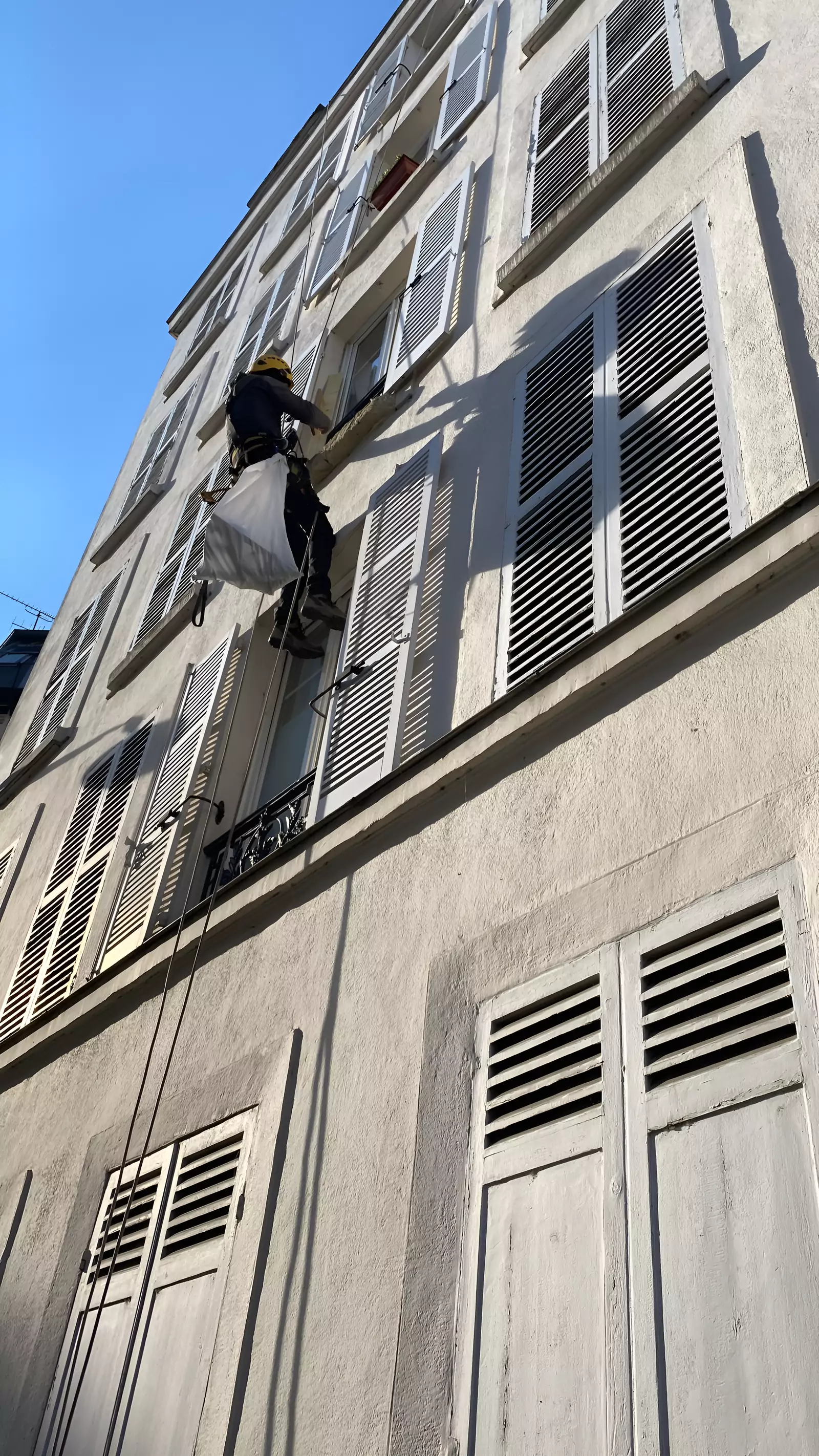 Cordiste avec un sac de chantier sur une façade à persiennes