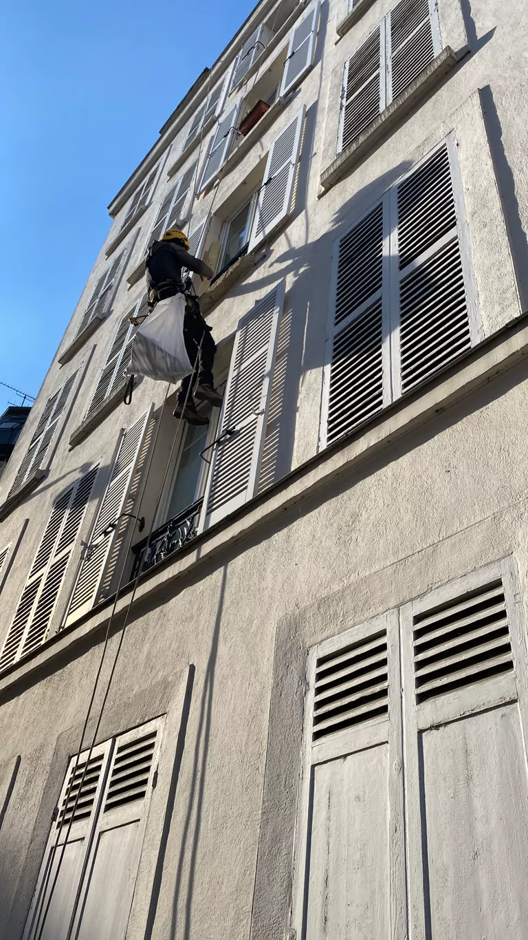 Cordiste avec un sac de chantier sur une façade à persiennes