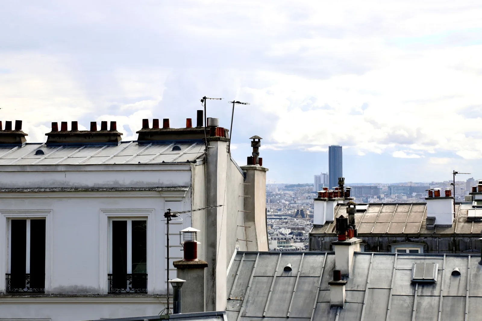 Toits en zinc d'immeubles parisiens avec souches de cheminée et lucarnes, vus depuis une toiture