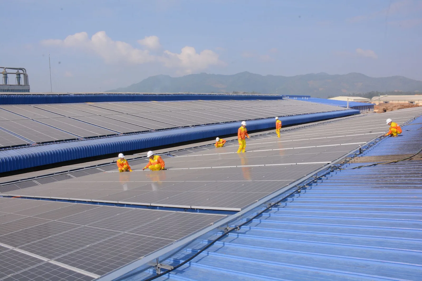 Toiture bac acier d'un bâtiment d'activité couverte de panneaux photovoltaïques, garde-corps de rive et techniciens sur le cheminement