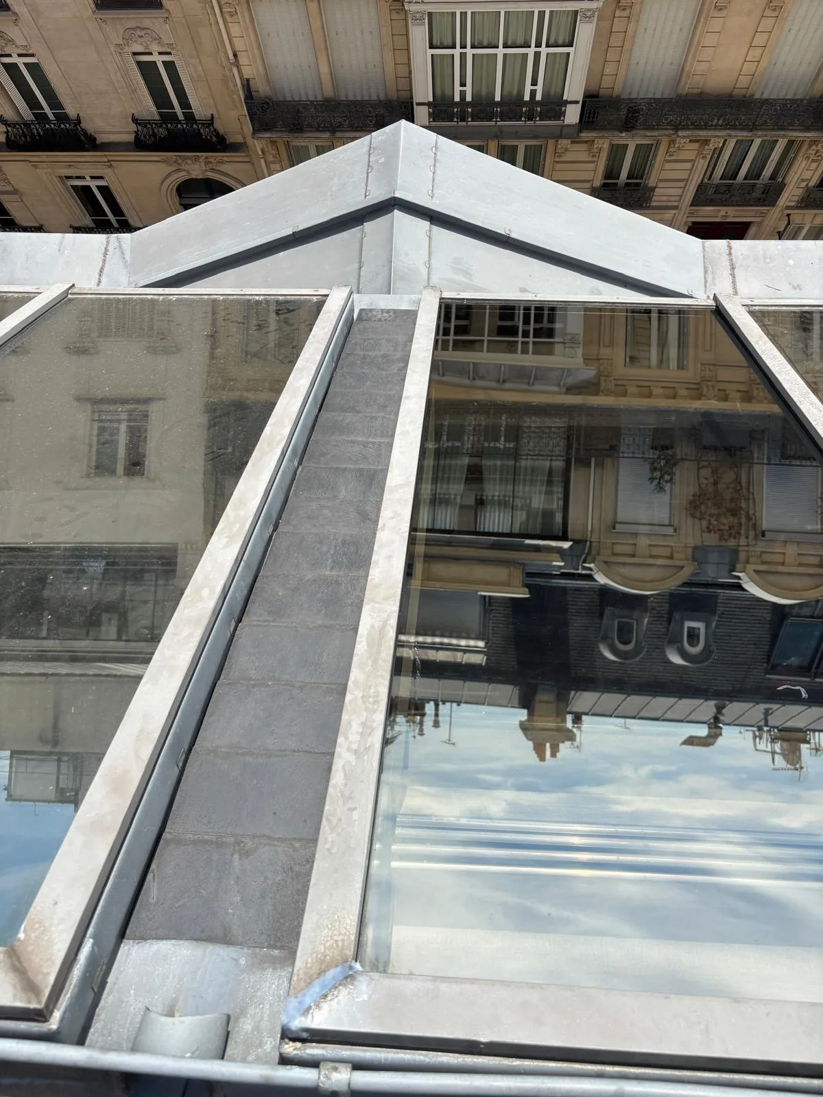 Verrière à châssis métalliques et zinguerie dans une cour d'immeuble, vue depuis les cordes